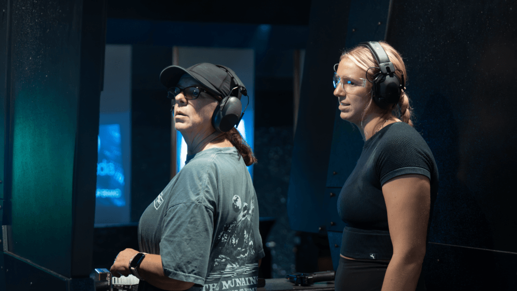 Two women ready to shoot at the range wearing proper attire and ear protection.