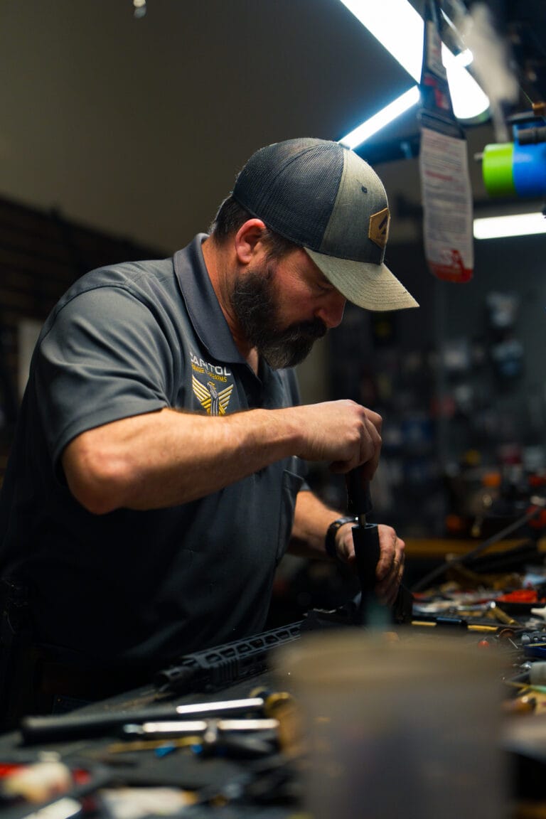 Man in a gray cap and polo shirt focusing on assembling a tool at a cluttered workshop workbench.